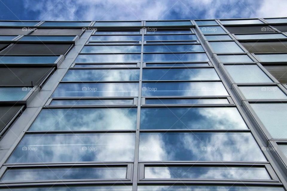 Bottom view of the glass facade of a building reflecting the sky