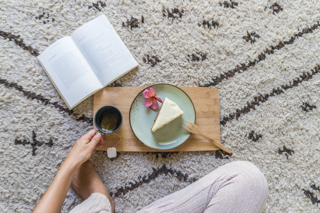 A girl enjoying a relaxing tea and slice of cake while reading a book sitting on a cozy Moroccan wool Beni Ourain rug. 
