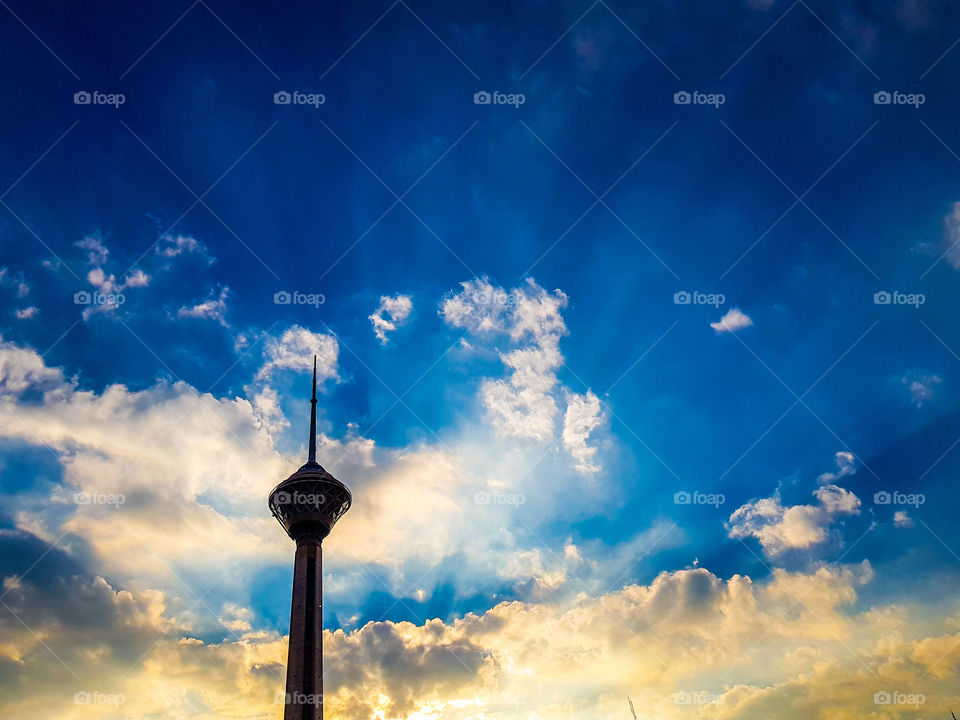 beautiful sunrise from behind the clouds early in the morning next to milad tower Tehran, as the sun's rays breakthrough and piercing through the dense clouds . they're called skyscraper for this scenery