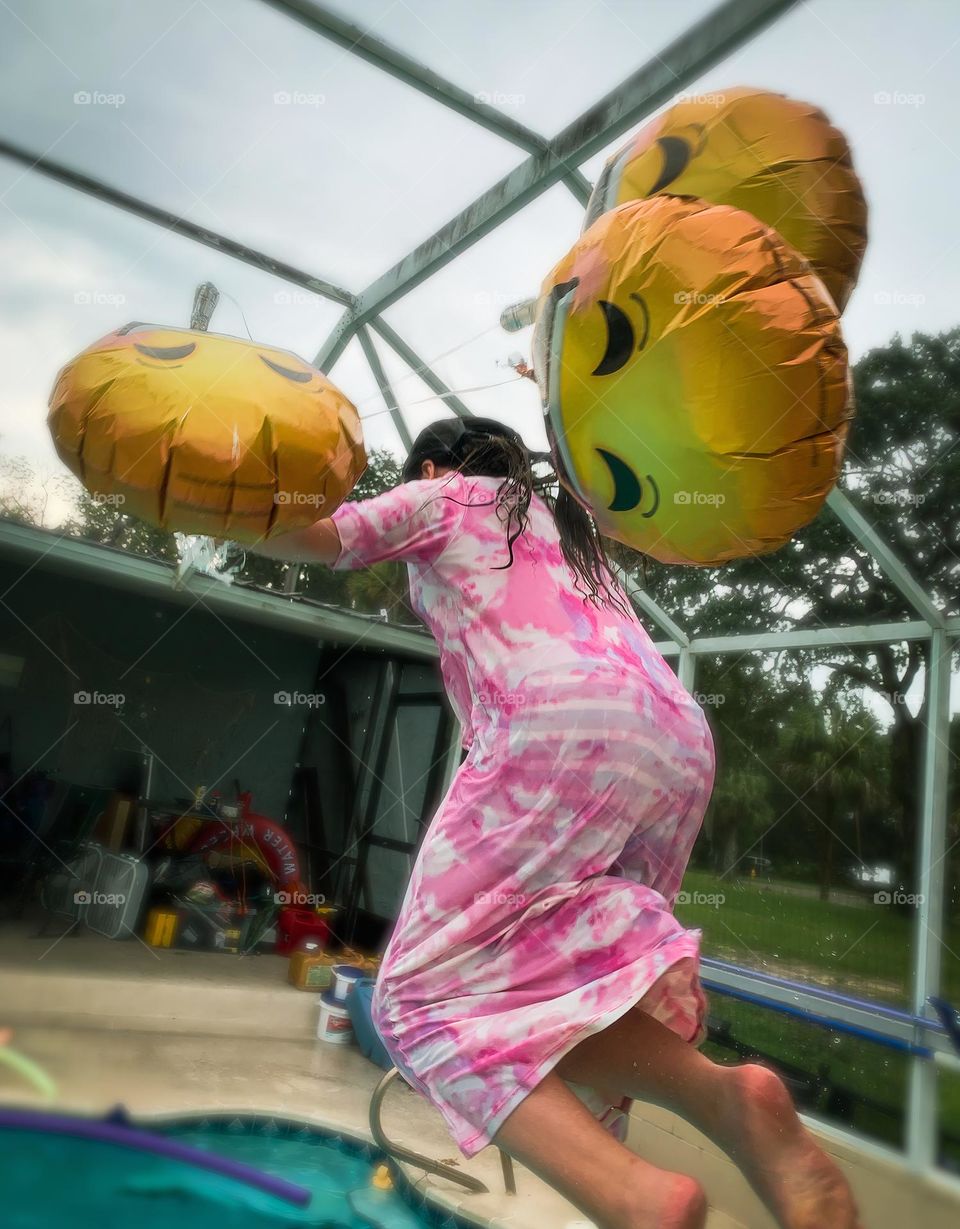 Smiley Faces Helium Balloons Seem To Pull The Girl Up In The Air While She Jumps In The Water With It In The Pool.