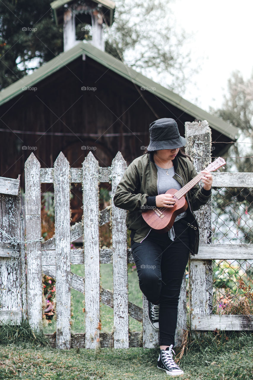 Girl playing a ukulele at the gate of a chapel in a rural village