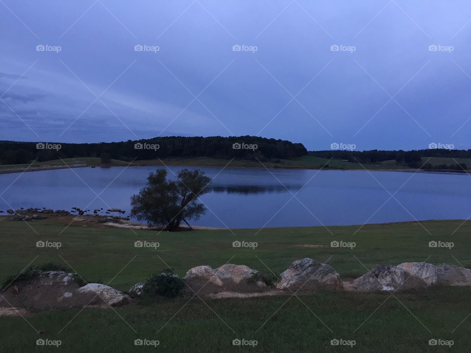 Beautiful scenery of trees reflecting upon the lake at dawn. Beautiful large rocks along the outer border.