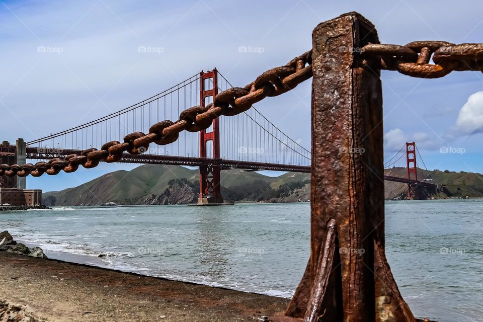 Looking at the Golden Gate Bridge through the rustic iron chain link guard rails with all their beautiful aged patina on a beautiful sunny day at Fort Point
