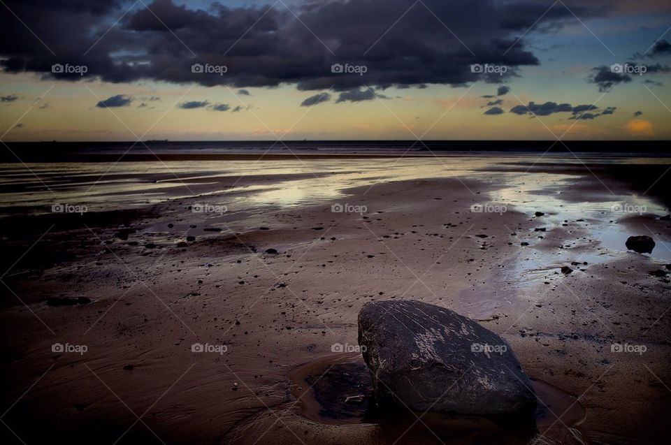 A large rock sits in the foreground on a beach in a storm.