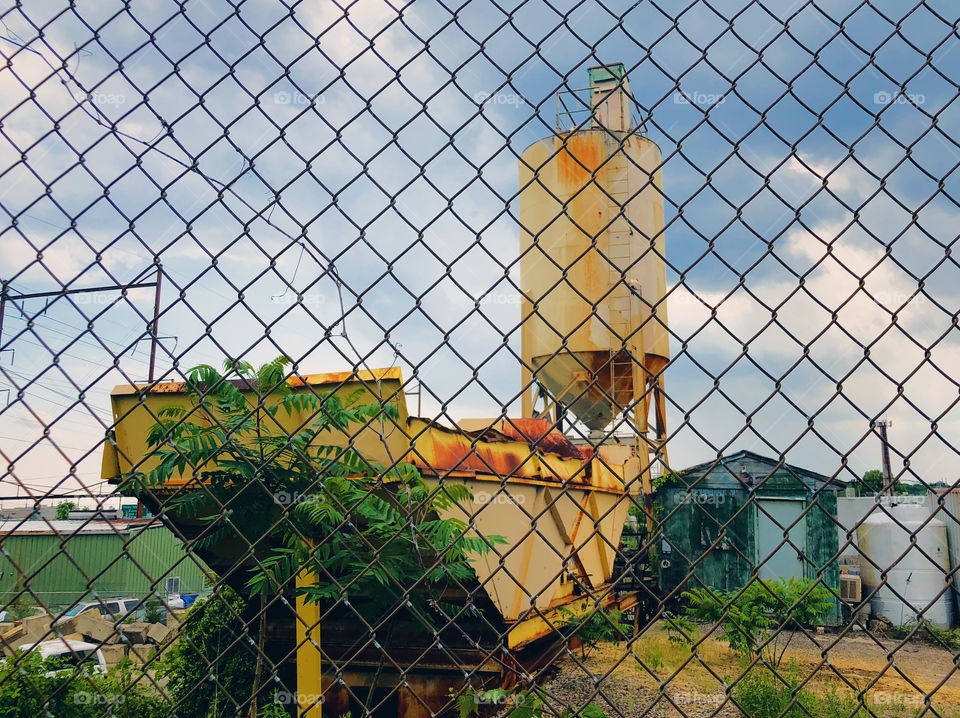 Rusty yellow water tank and shed outdoors behind chain link fence.