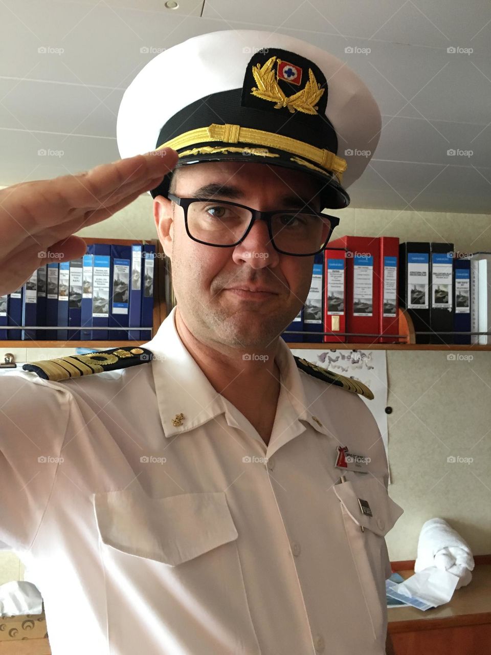 Cruise ship captain wearing hat saluting in his office.