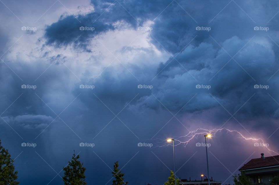 Lightning touches two street lamps during a thunderstorm under a dark cloudy sky