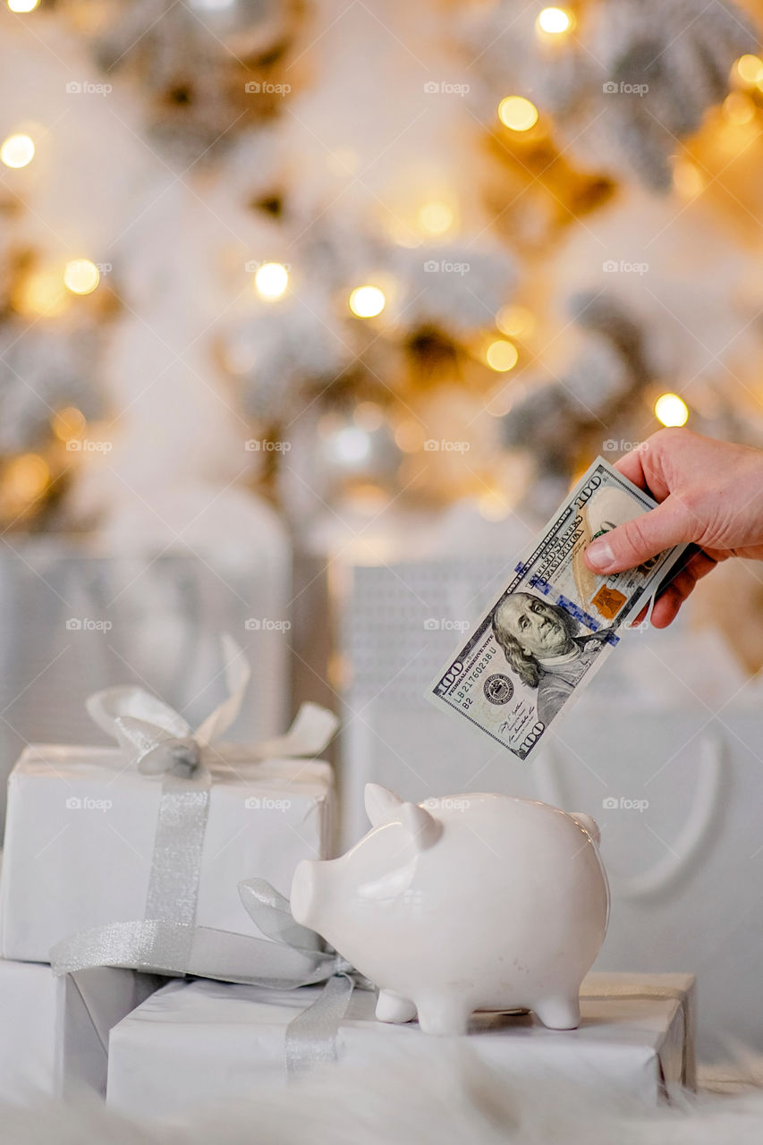 piggy bank with 100 dollars banknote in festive New Year atmosphere of scenery. Magical bokeh with Christmas tree and bright lights.