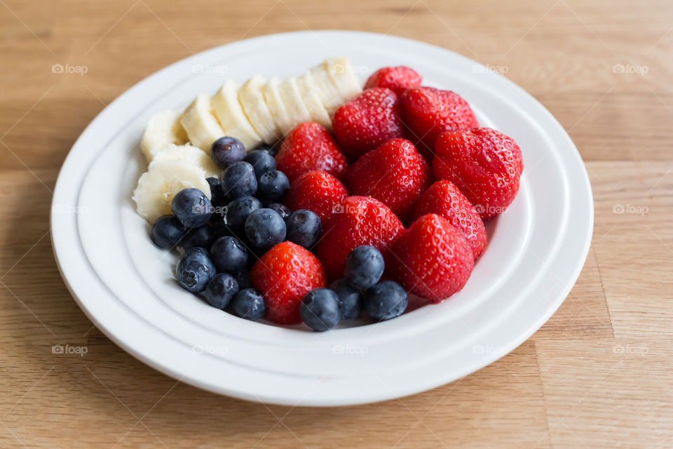 Healthier snacks, fresh blueberries, strawberries and banana on white plate 