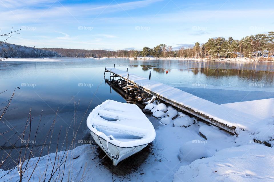 Boat and wooden pier covered with snow on a beautiful sunny cold winter day by frozen lake 