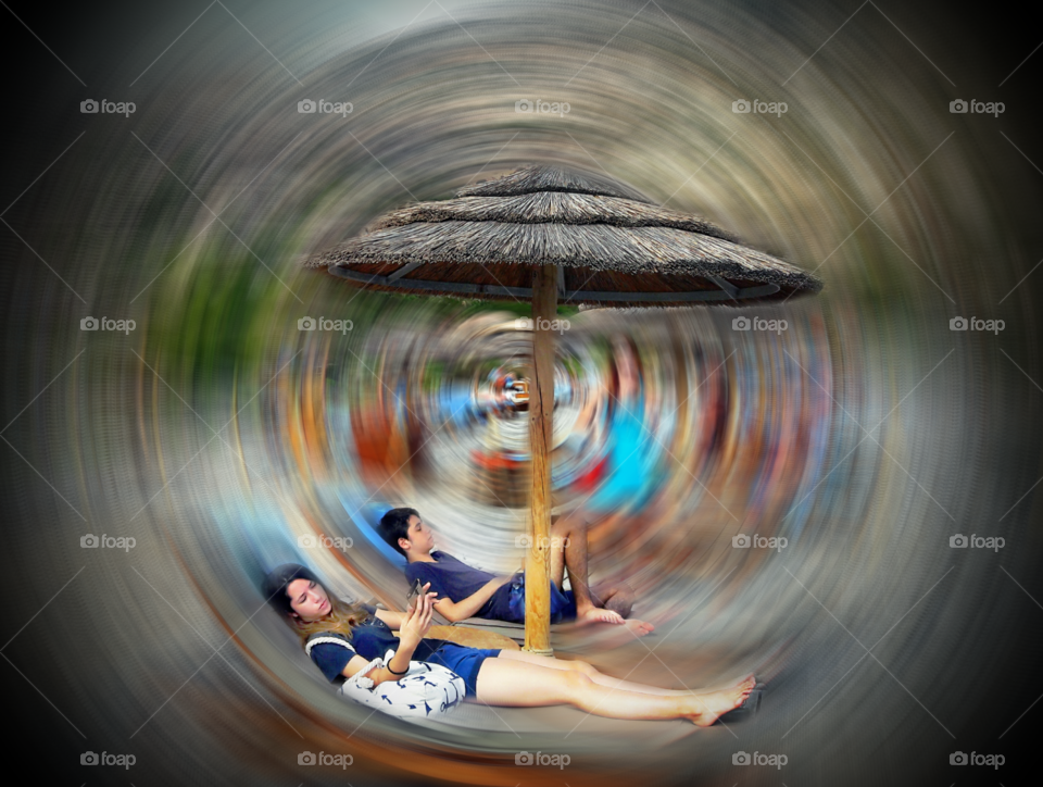 Blurred motion of young man and woman lying under beach umbrella