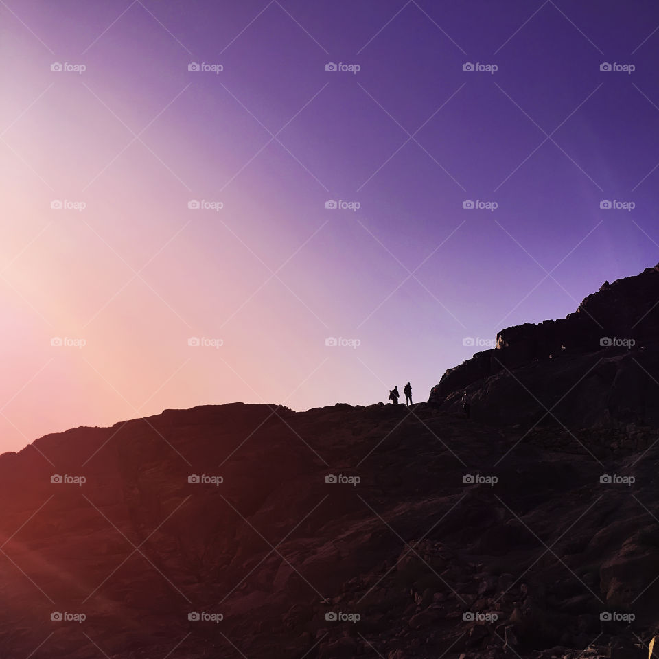 Two silhouettes of people hiking at the mountains at sunrise time 