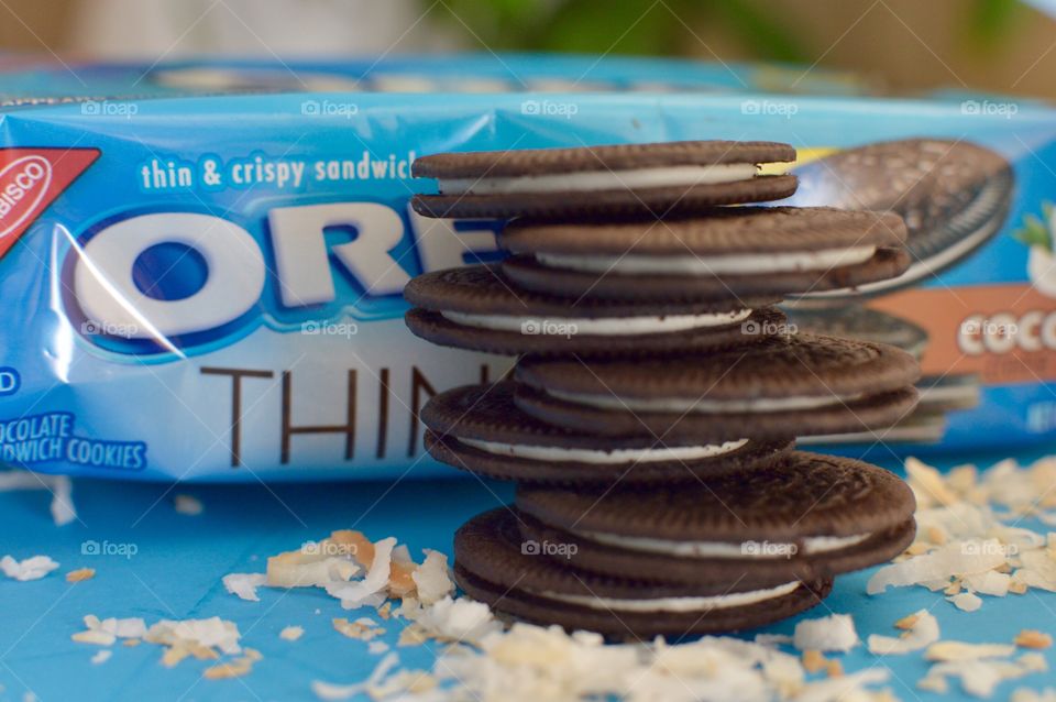 A stack of coconut Oreo thin cookies on a blue background with coconut shreds