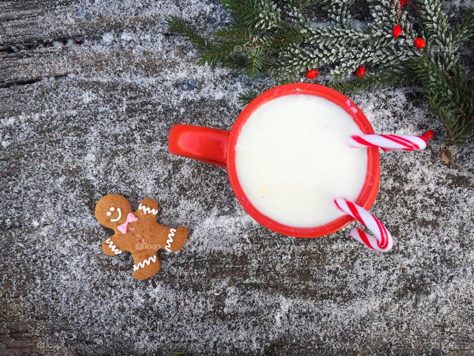 Red cup of white chocolate and candy canes inside with a gingerbread man beside on snowy table