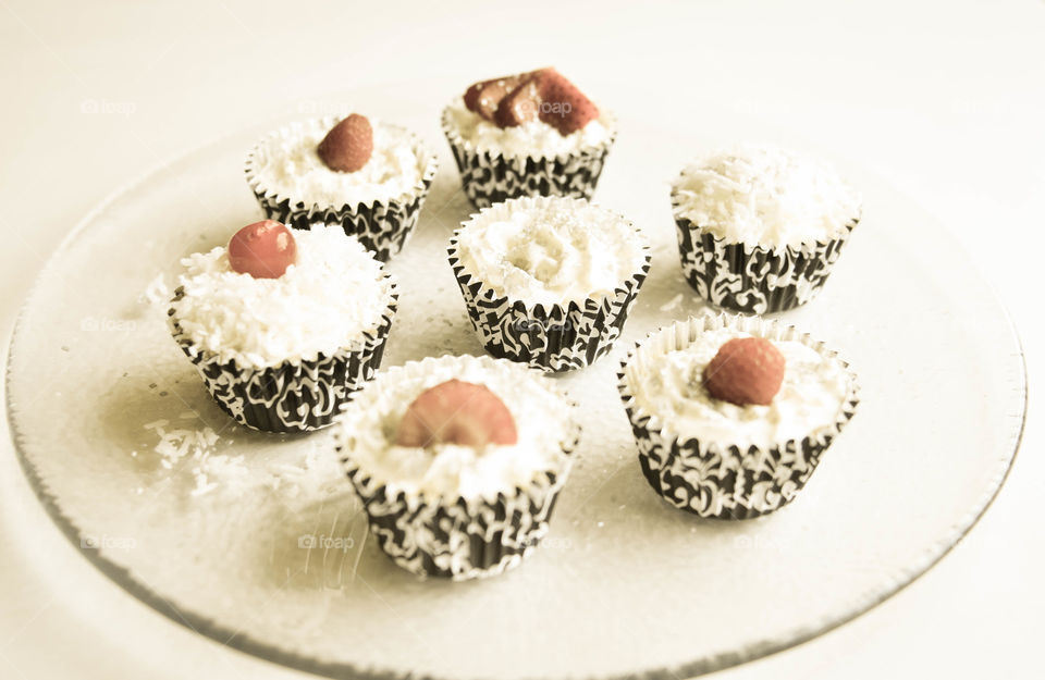 Vintage style picture of mini cupcakes topped with whipped cream, coconut shavings, and berries