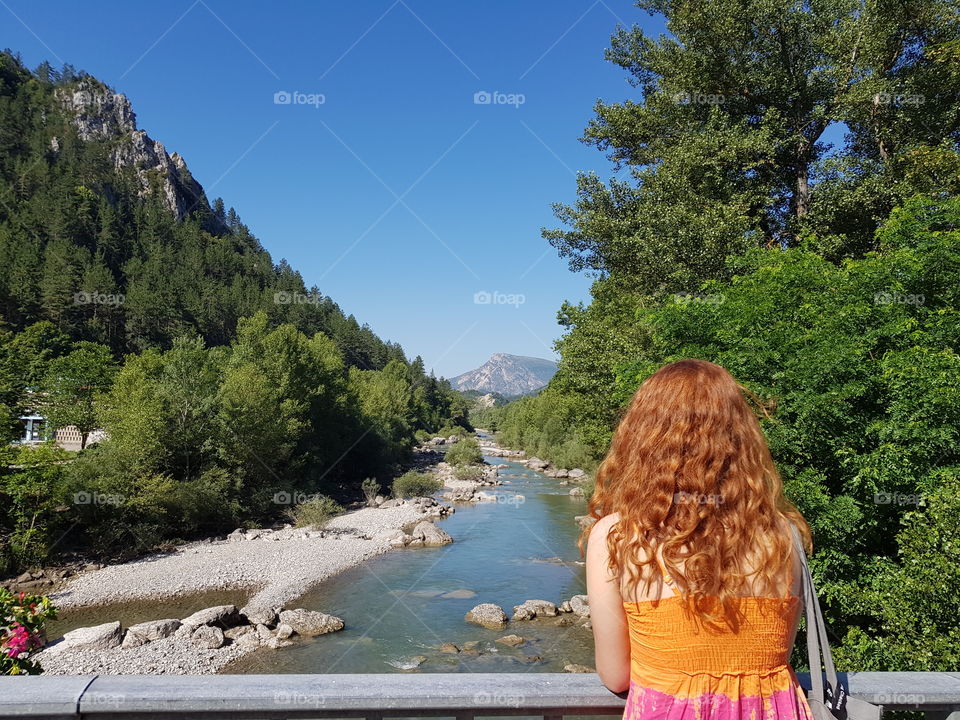 Young redhead woman looking out at Verdon river in Castellane,  France.