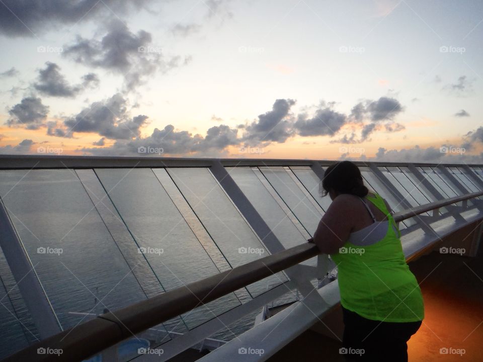 Adult female watching the sun rise over the water on a cruise ship