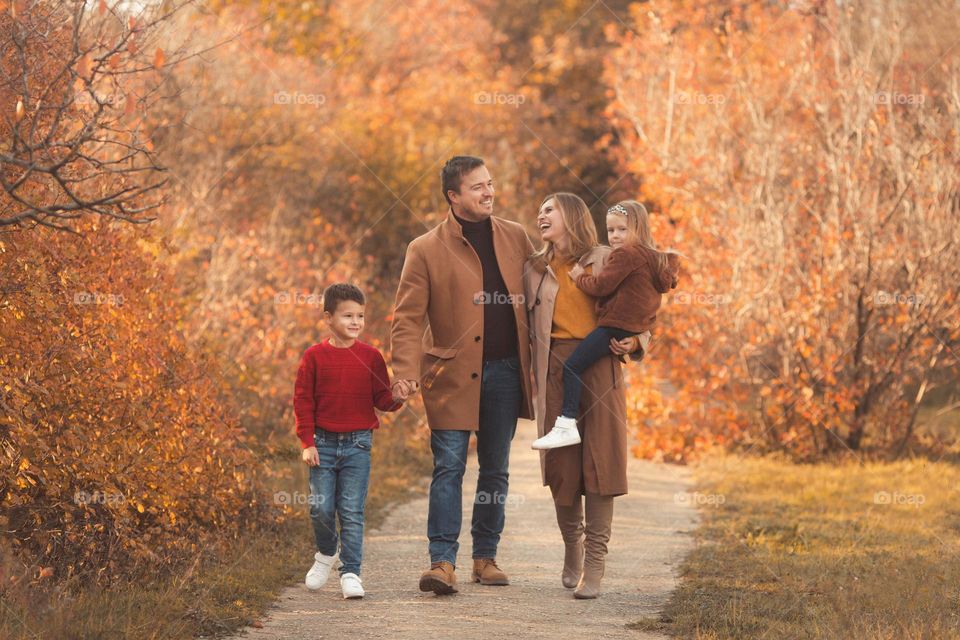 Happy family in stylish clothes walking in cozy autumn park with orange leaves 