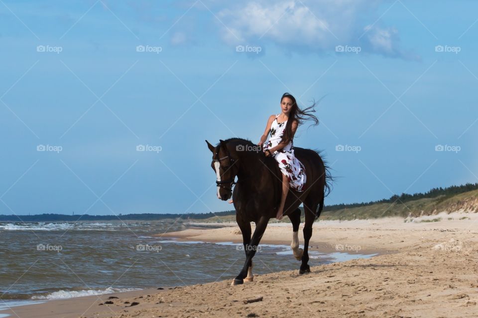 Pretty woman riding horse at beach