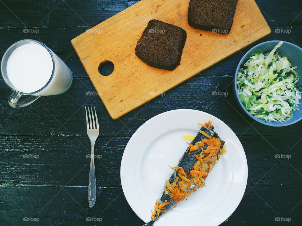 baked mackerel, vegetable salad, a cup of milk and bread on a black background, breakfast