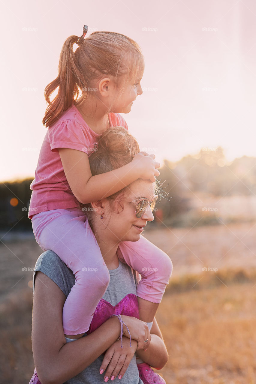 Sisters enjoying piggyback ride. Teenage girl carrying her younger sister up on the back and shoulders spending time playing together outdoors in the countryside. Candid people, real moments, authentic situations