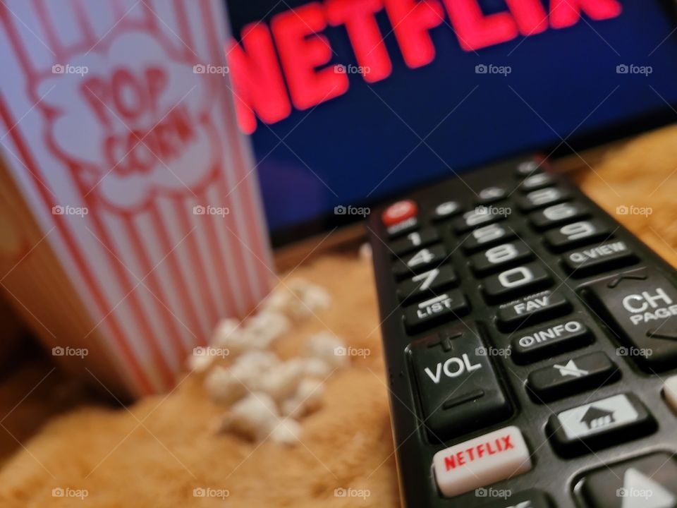 Aiming the remote control at television screen to choose favorite netflix channel to binge watch TV shows or movies for a fun and cozy evening in with a popcorn snack