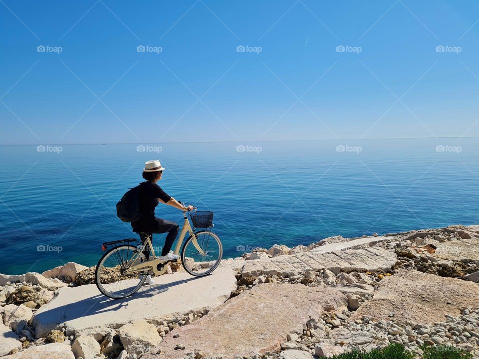 woman from behind with hat pedaling on the rocks of the "Costa dei Trabocchi" in Italy