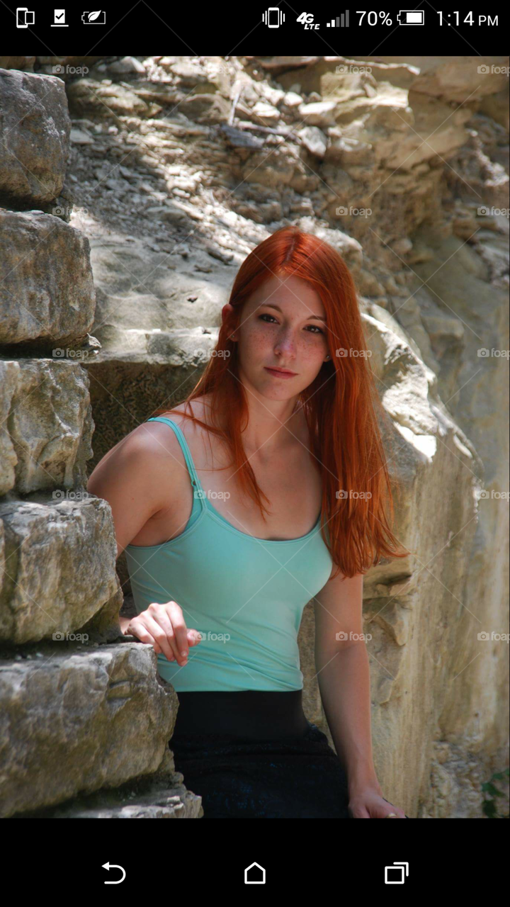 redhead woman leaning against stone wall in forest