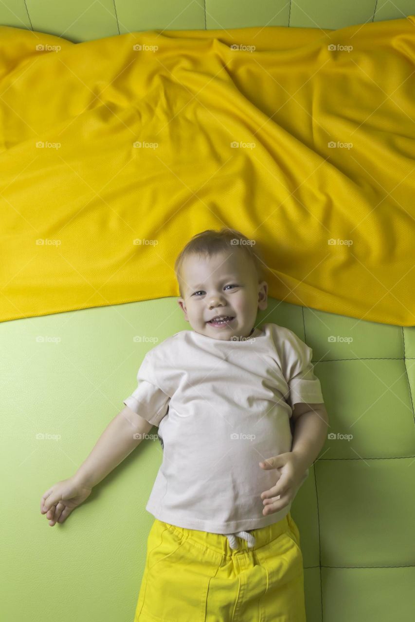 A portrait of a child sitting at home on a green sofa depicts different emotions in yellow shorts.