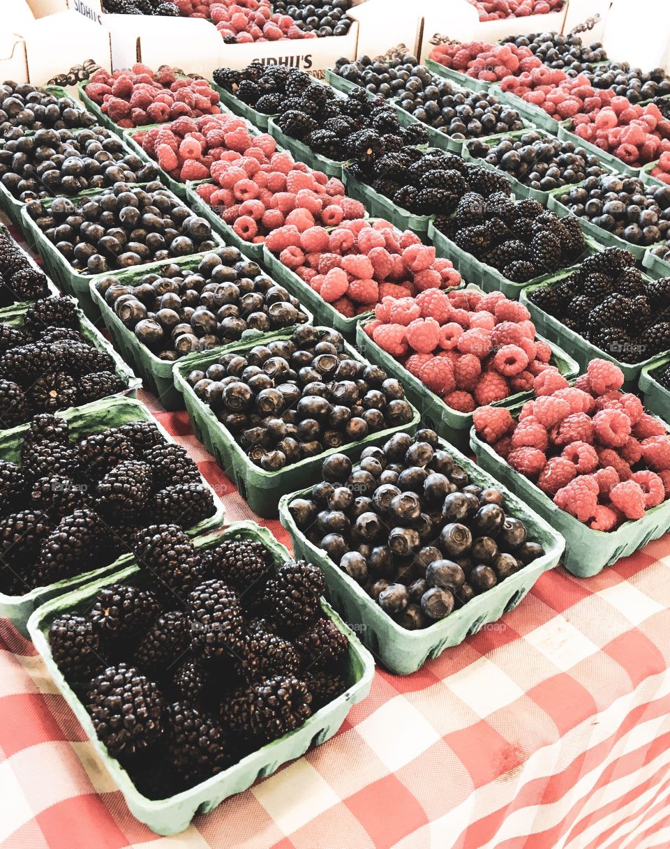 Blackberries, Raspberries, and Blueberries for sale at the market on a plaid red and white tablecloth