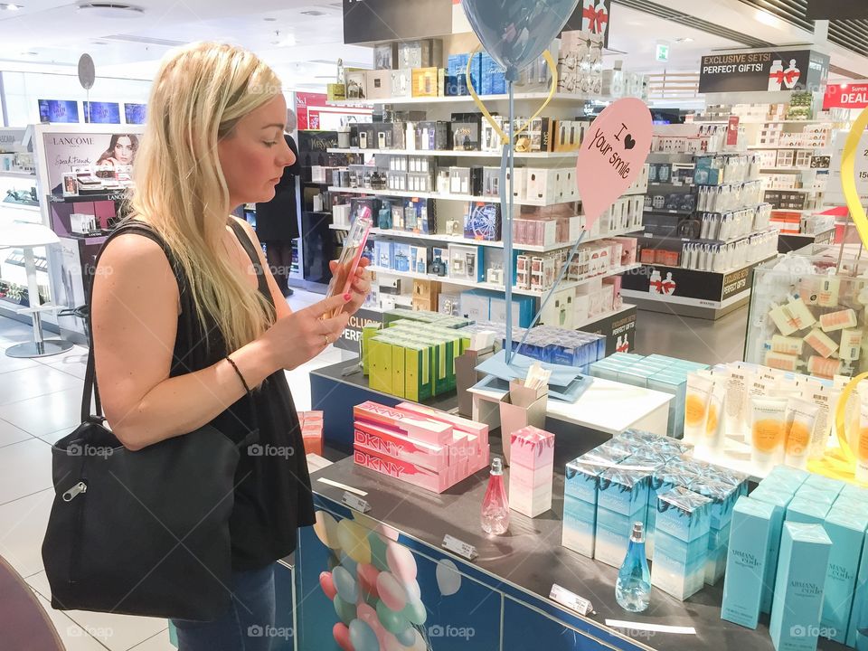 Young woman in her 30 years is smells perfume in a Taxfree shop at Copenhagen airport in Denmark.