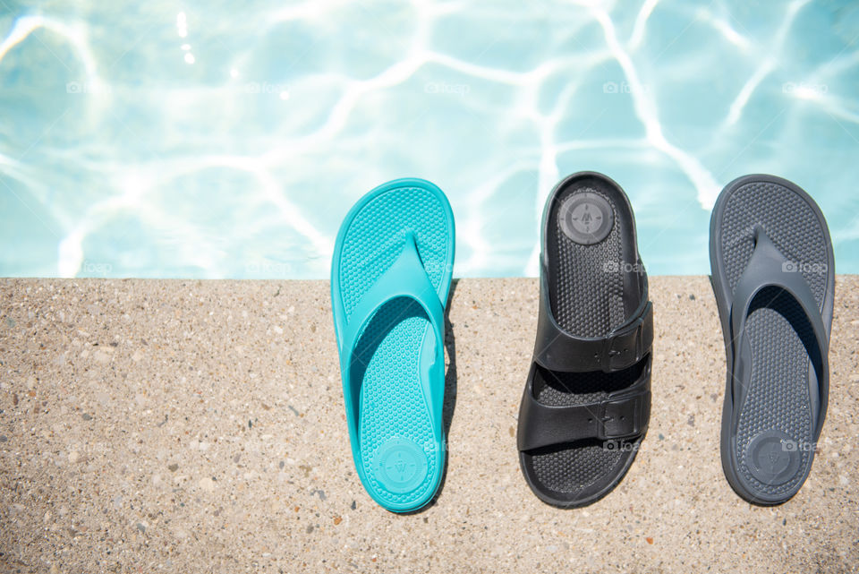 Flat lay of women's sandals on the ledge of an outdoor swimming pool