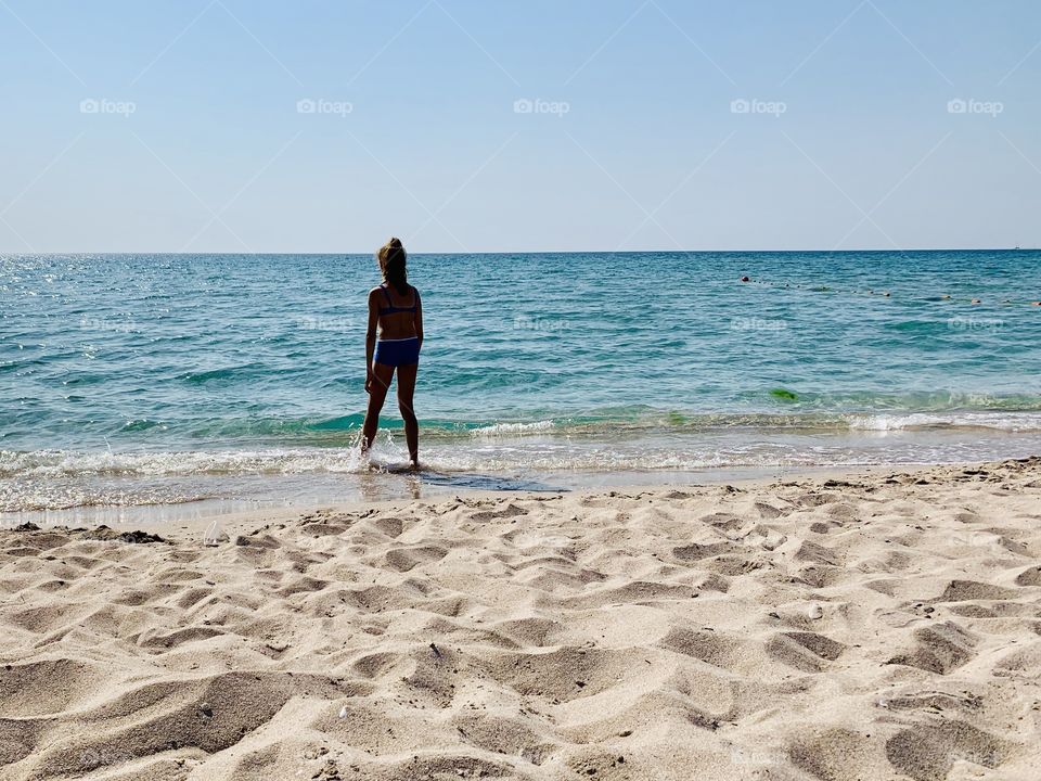 Girl and the sea. Sandy beach and azure-colored sea water.