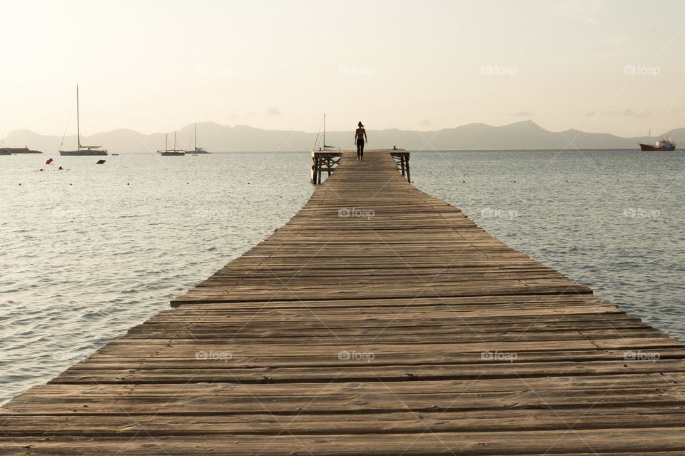 Woman taking an early morning walk on wooden pier in the ocean at sunrise 
