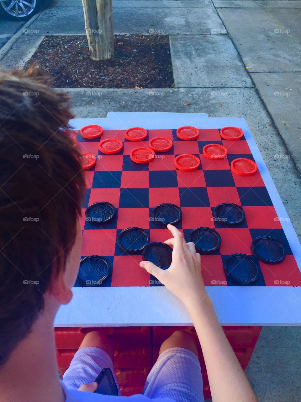 Back view of teen playing checkers outside on sidewalk 