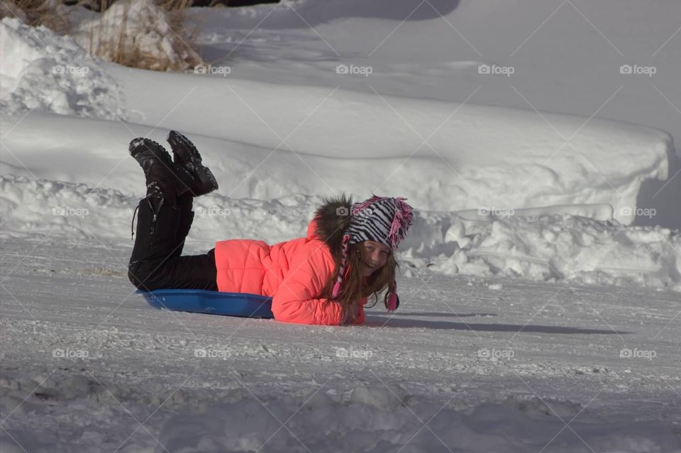 A young girl sled riding down a hill on a tiny sled.