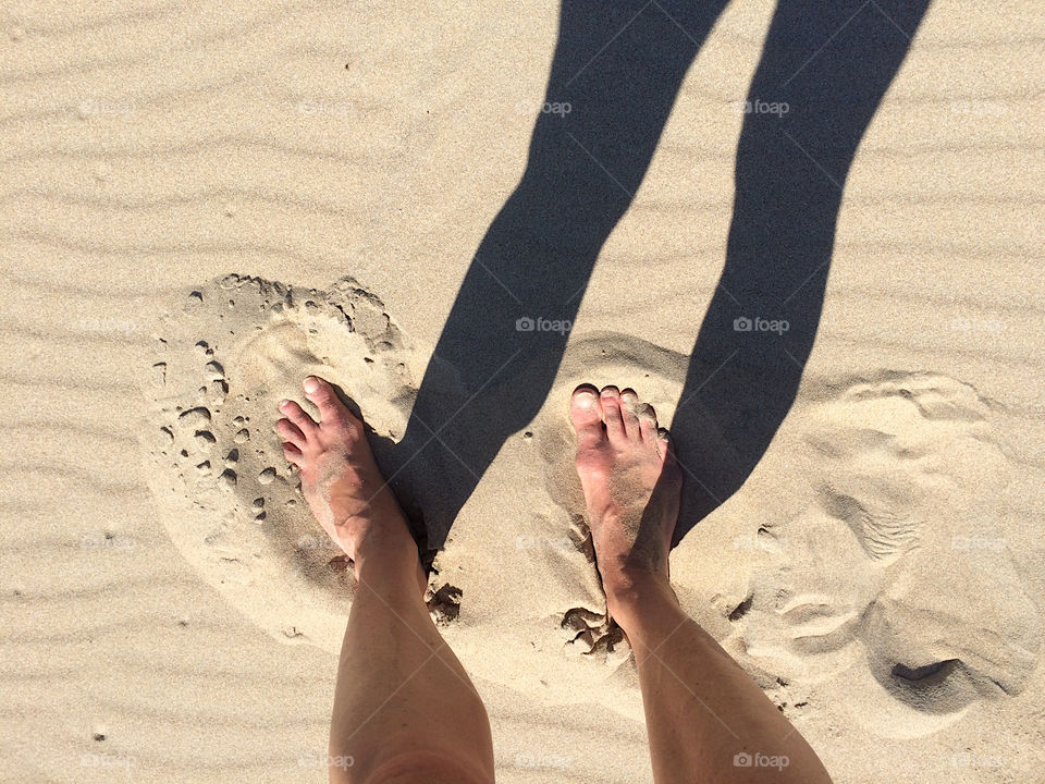 Barefoot on the beach with shadow of my legs. 