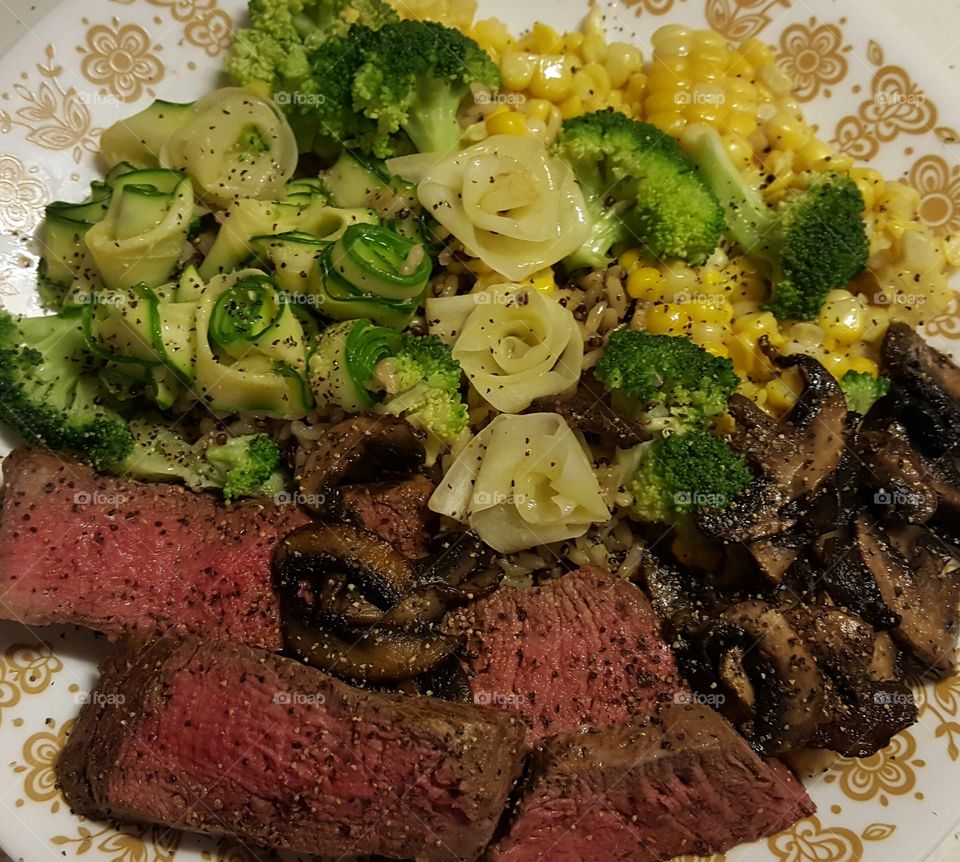 Sliced beef tenderloin, with steamed veggies including zucchini, white carrot, broccoli, mushrooms, corn, all over Seeds of Change garlic quinoa.