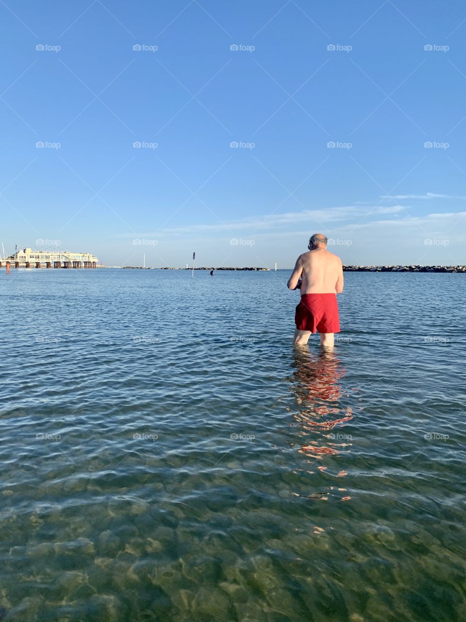 a man in a red bathing suit seen from behind takes a bath in the sea