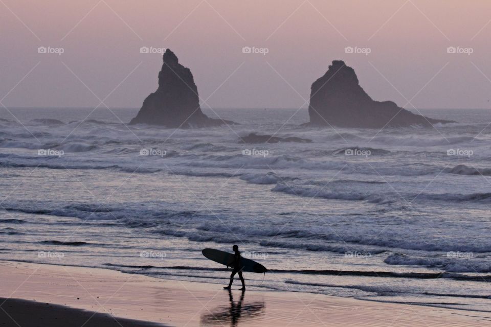 Lone surfer walking on beach during a sunset 