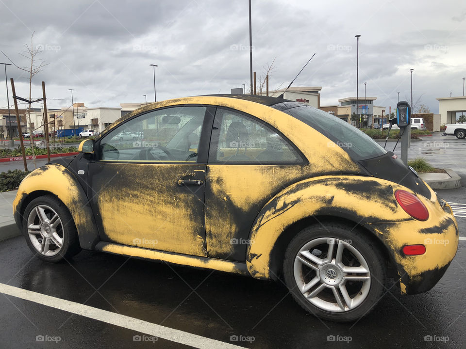 Dirty yellow bug in a parking lot on a cloudy day. 