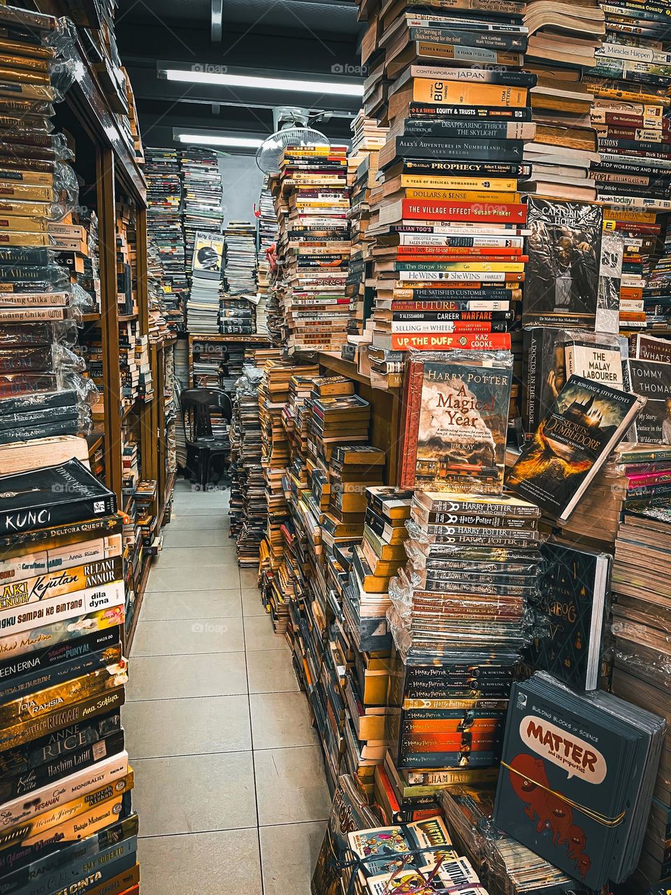 Stacked of books in a used bookstore and a narrow pathway to enter the bookstore 