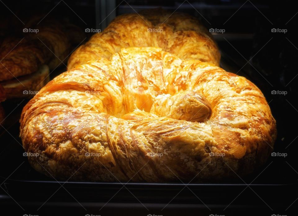 Fresh croissant in a display cabinet for sale in a local cafe shop. The food item is lit by a single source lighting.