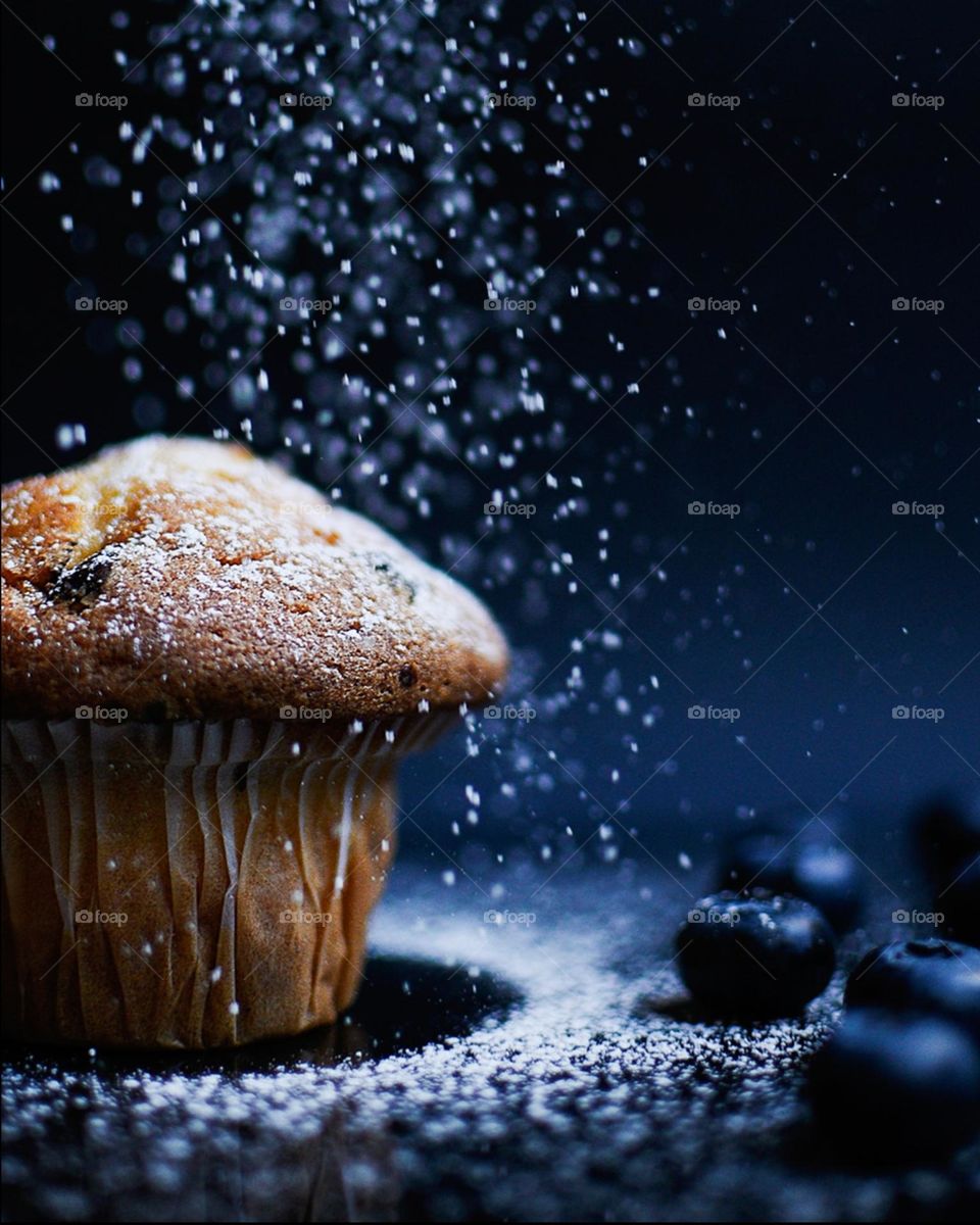 Christmas blueberry muffin on black background sprinkled with white icing suger looks like snow