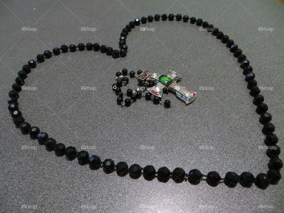 On a gray background are black agate beads in the shape of a heart, and in the center is a large cross with rhinestones and ruby.