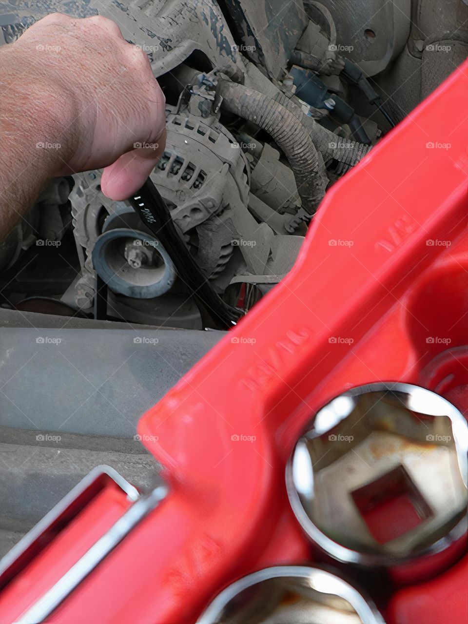 Under the hood of a red pickup truck with combination wrench set tools organized in a red tool hard case by the work station and the mechanic handyman fixing a piece close-up macro.