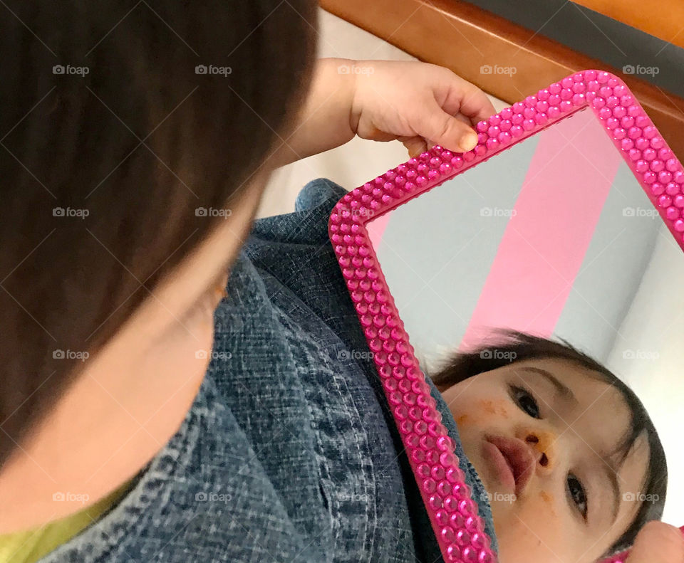 Baby girl with messy face looking in a mirror