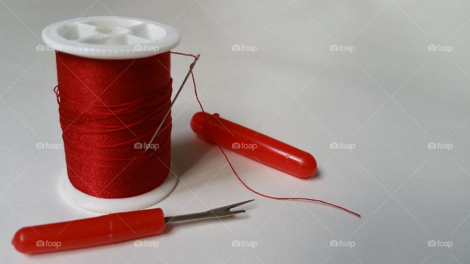 Red sewing thread, needle and seam ripper