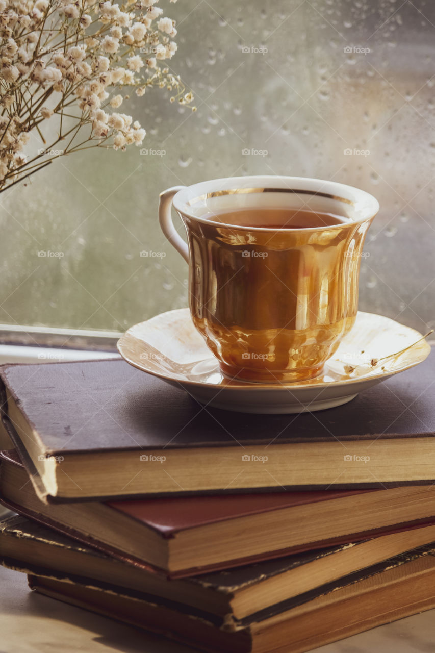 a cup of tea on the books in front of rainy window