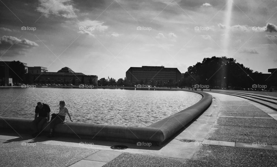 Relaxing couple sitting on the banks of the water mirror of The Capitol